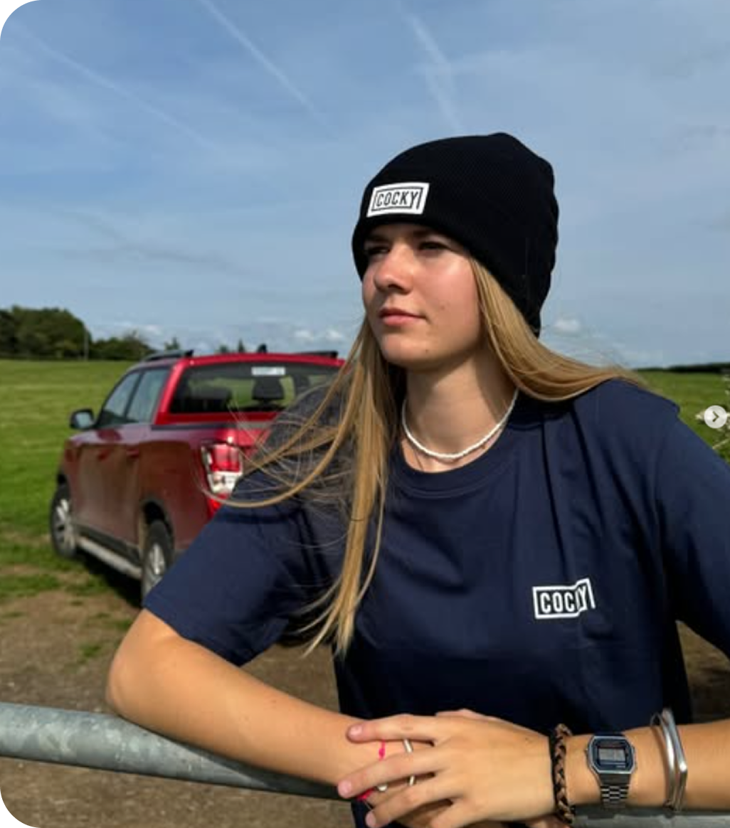 woman wearing Cocky beanie and tee, leaning against fence